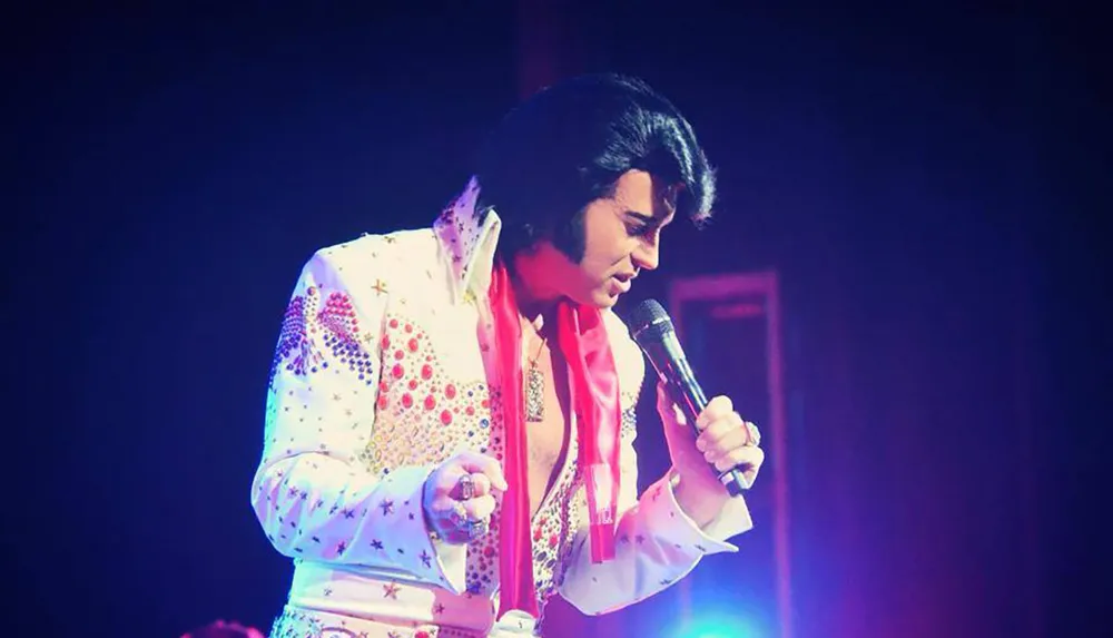 A person dressed in an elaborate white and red jumpsuit is performing on stage with a microphone in hand