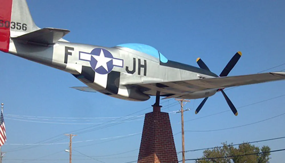 The image shows a P-51 Mustang a World War II-era fighter aircraft mounted on a pedestal for display under a clear sky