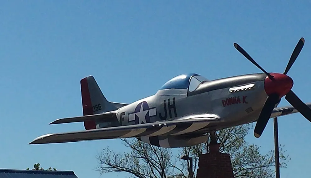The image shows a vintage military aircraft specifically a P-51 Mustang on display under a clear blue sky