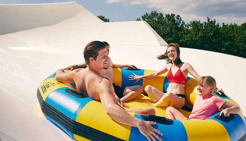 Three people are enjoying a sunny day at a water park sliding down in a large inflatable ring with big smiles on their faces