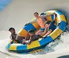 A group of people are enjoying a ride on an inflatable raft down a water slide with an inset showing a person smiling on a single-person tube