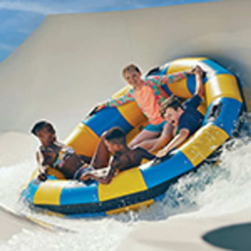 Four people are enjoying a ride down a water slide in a large inflatable raft