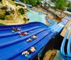 Three people are enjoying a sunny day at a water park sliding down in a large inflatable ring with big smiles on their faces