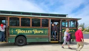 People are boarding a trolley-style tour bus on a sunny day.