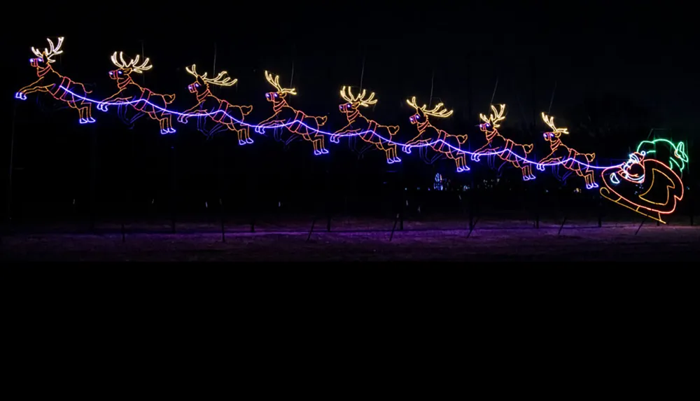 A festive display of neon lights features Santa Claus in a sleigh being pulled by eight reindeer against a dark background