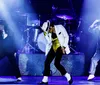 Three performers onstage exhibit a dynamic dance pose reminiscent of Michael Jacksons iconic style with the central figure donning a white jacket and gold belt