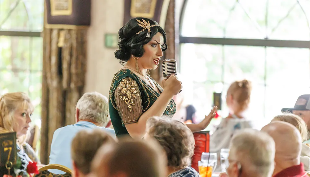 A performer in a vintage-style outfit sings into a microphone while interacting with an audience in a decorated venue