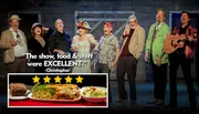 A group of eight people in colorful attire is joyfully posing on a stage, with one person holding a guitar and another with a unicycle.