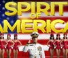 The image features a group of performers in red costumes and a naval officer in front of an American flag backdrop with the text SPIRIT OF AMERICA and a partial view of the Statue of Liberty