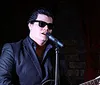 A person wearing sunglasses is singing into a microphone on stage