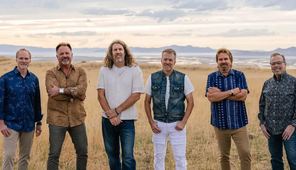 Six men are standing together in a grassy field with a scenic mountainous background
