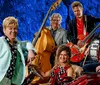 A group of five musicians poses with their instruments in front of a blue textured background