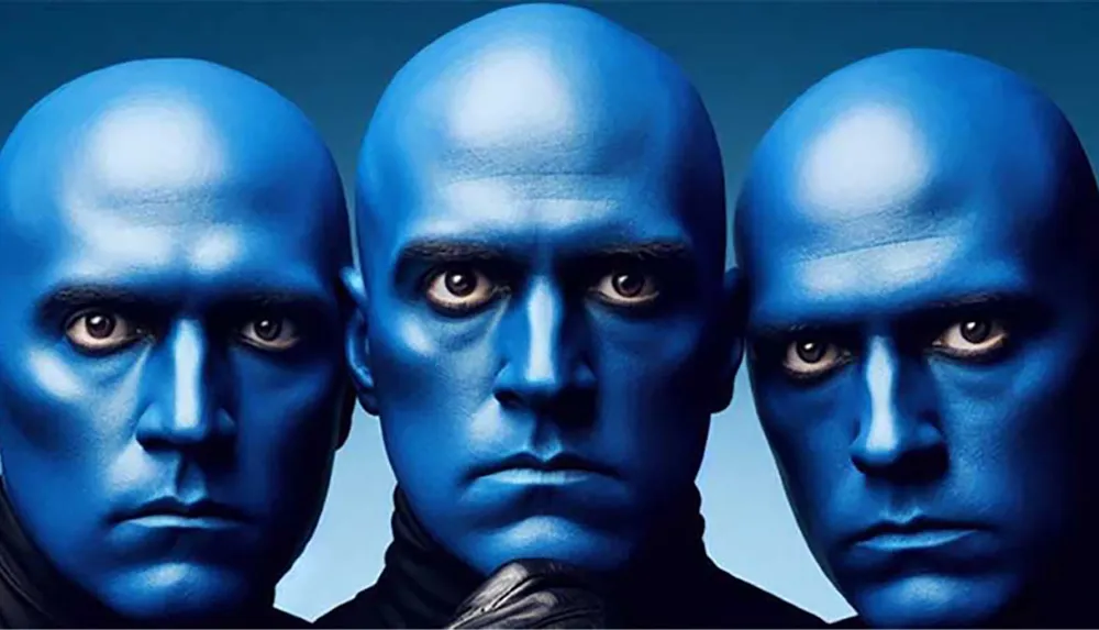 Three individuals with completely blue-painted skin and blank expressions are closely aligned in the image