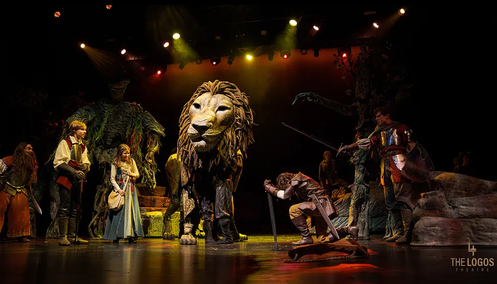 A theatrical performance features a large majestic lion puppet surrounded by actors in medieval costumes on a dimly lit stage