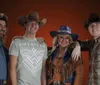 A group of four people wearing cowboy hats and casual Western-style clothing pose together in front of a warm-toned background