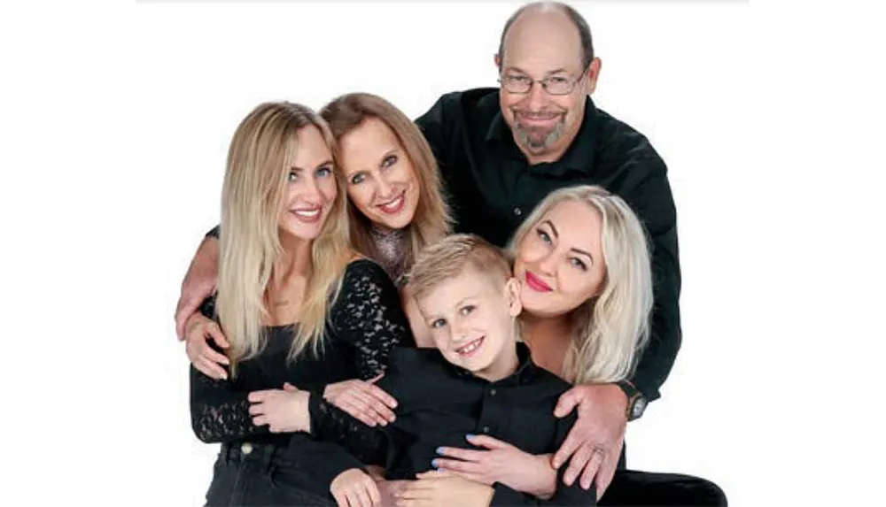A family of five including two men two women and a child is posing closely together and smiling in a family portrait