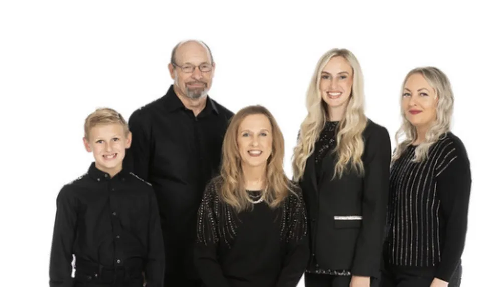 A group of five people dressed in black are posing together against a plain white background