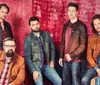 Five men in casual outfits are posing in front of a red and blue tie-dye background