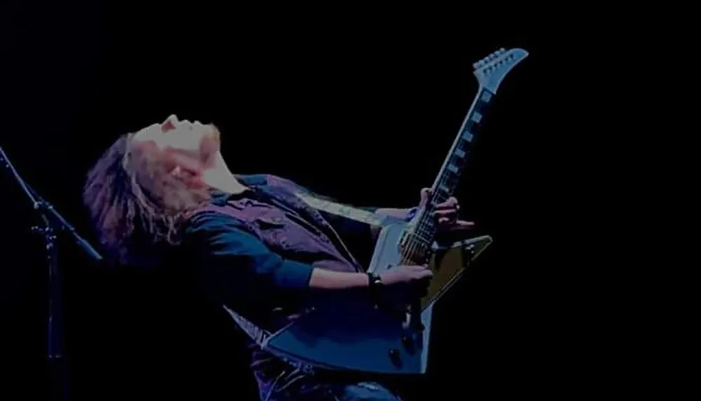 A musician passionately plays an electric guitar on stage leaning back dramatically