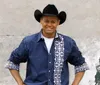 A musician in a cowboy hat stands with arms open on stage surrounded by a band performing for an enthusiastic crowd