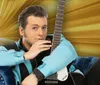 A man in a blue and black outfit is reclining on a blue sofa with a guitar next to a vibrant RocknRoll SUN Rise sign