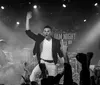 A band performs energetically on stage with a lively audience as the lead singer raises his hand in excitement