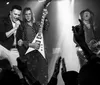 A band performs energetically on stage with a lively audience as the lead singer raises his hand in excitement