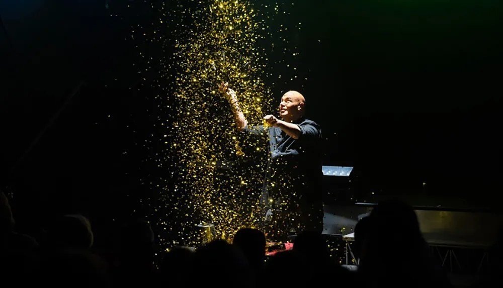 A performer captivates an audience by throwing a shower of golden glitter in a spotlight