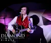 The image shows a performer dressed in a star-spangled outfit singing with a microphone next to the text A Neil Diamond Tribute