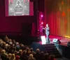 Two people are on a stage with one wearing a sparkly jacket and the other laughing in front of a backdrop that says THA Mentalist Guy with red curtains above