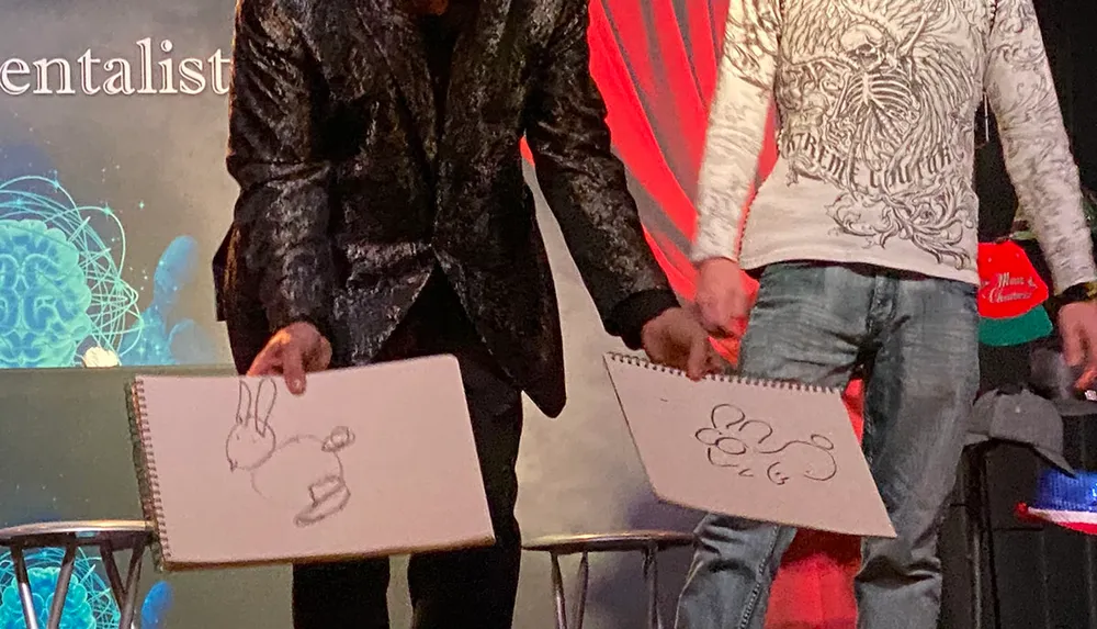 Two people are holding sketchpads with drawings of rabbits on stage