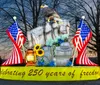 The image shows a glowing lantern sculpture of a farmer in front of a covered wagon surrounded by large illuminated flowers and barrels set against a dark wooded background