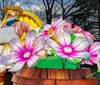 The image shows a glowing lantern sculpture of a farmer in front of a covered wagon surrounded by large illuminated flowers and barrels set against a dark wooded background