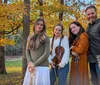 A group of four people are playing musical instruments and singing outdoors in a scenic field with mountains in the background