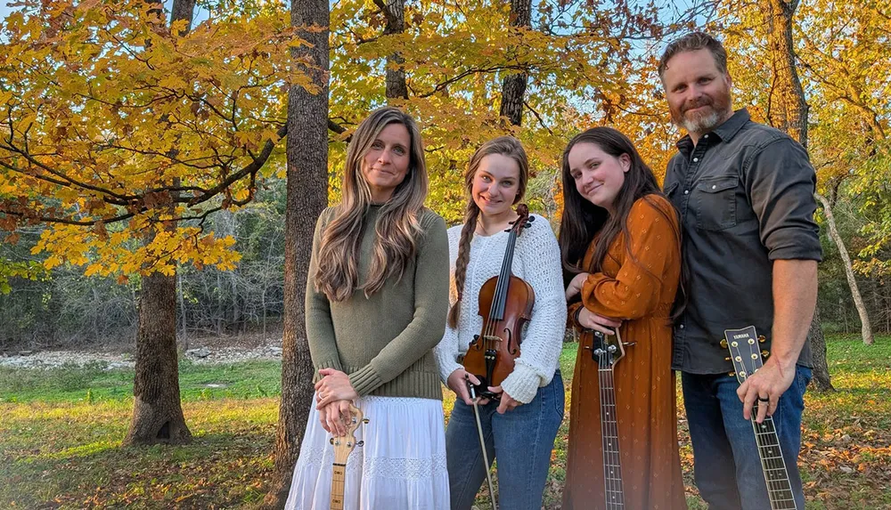 A family stands together in an autumn forest holding various musical instruments