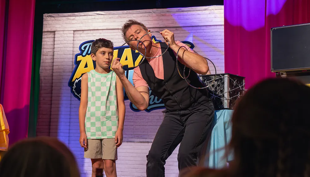 A magician performs a trick with rings next to a young boy on stage