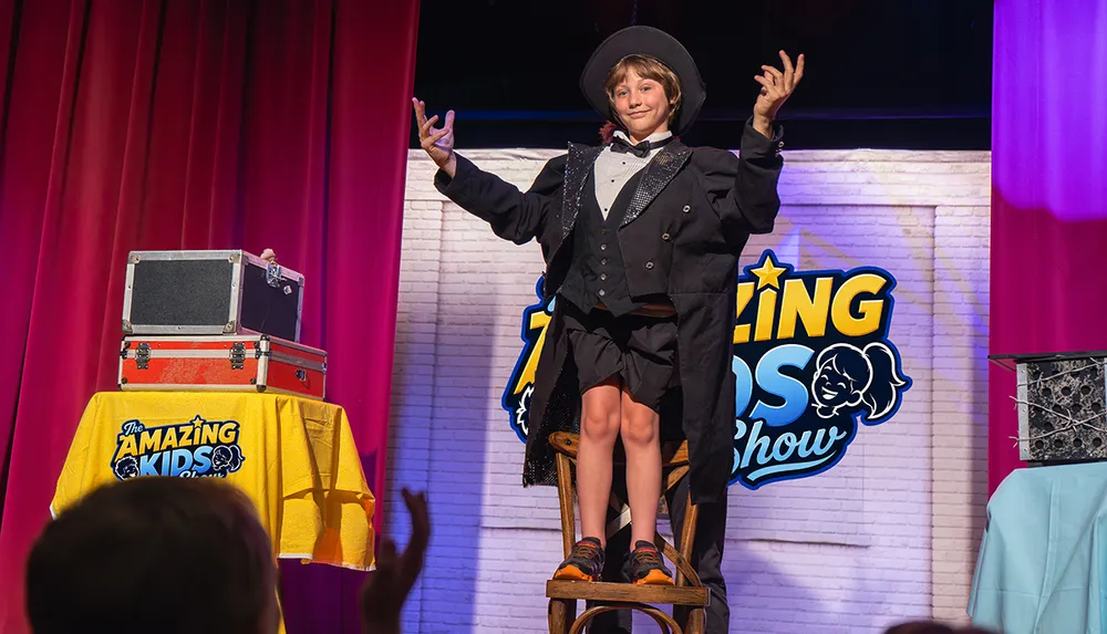 A child dressed as a magician performs confidently on stage at The Amazing Kids Show