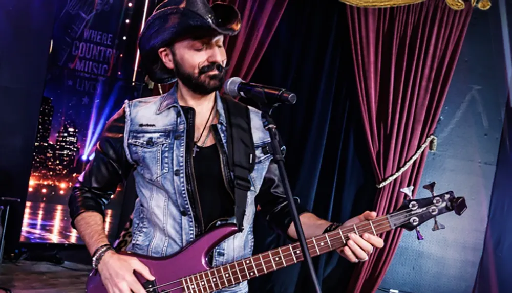 A musician wearing a cowboy hat and denim jacket is playing a purple electric guitar on stage