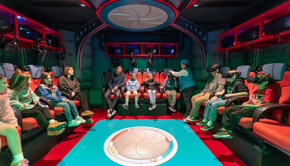 People are seated in a futuristic vibrant room some wearing virtual reality headsets while a staff member assists another guest