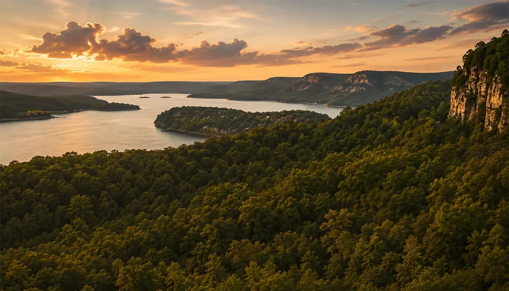A scenic landscape shows a sunset over a forested hillside leading down to a large lake with distant mountains