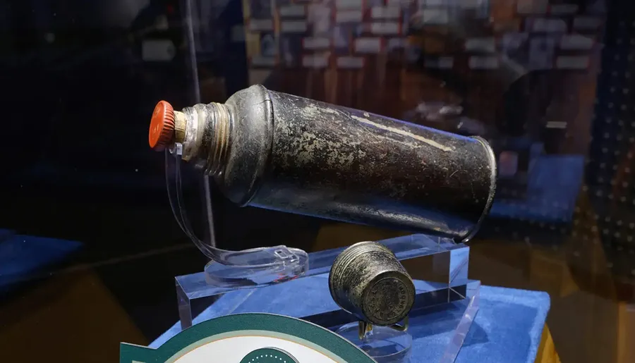 A vintage metal container with a red cap is displayed on a stand, likely in a museum setting.
