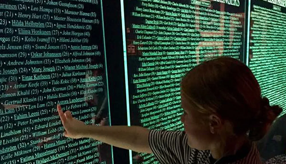 A person is pointing at a panel with a list of names which appears to be a memorial or informational display