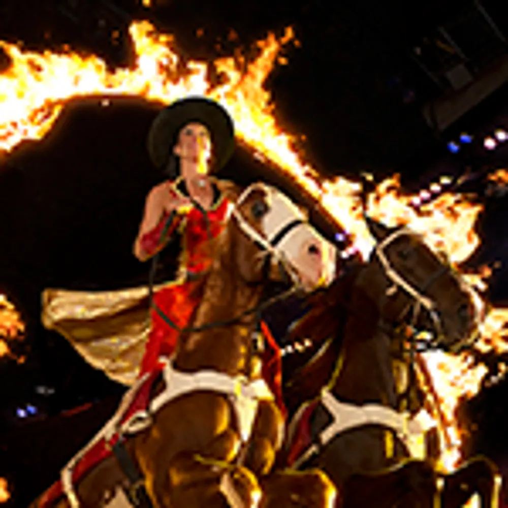 A performer in a red outfit rides a horse through a ring of fire