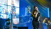 A singer performs on stage with a band during a live concert, with dynamic lighting and a winter-themed backdrop.