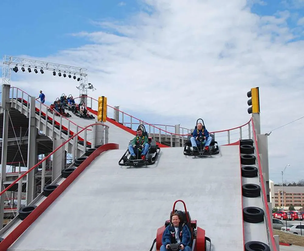 Participants are riding go-karts down a steep curved track in an outdoor karting facility