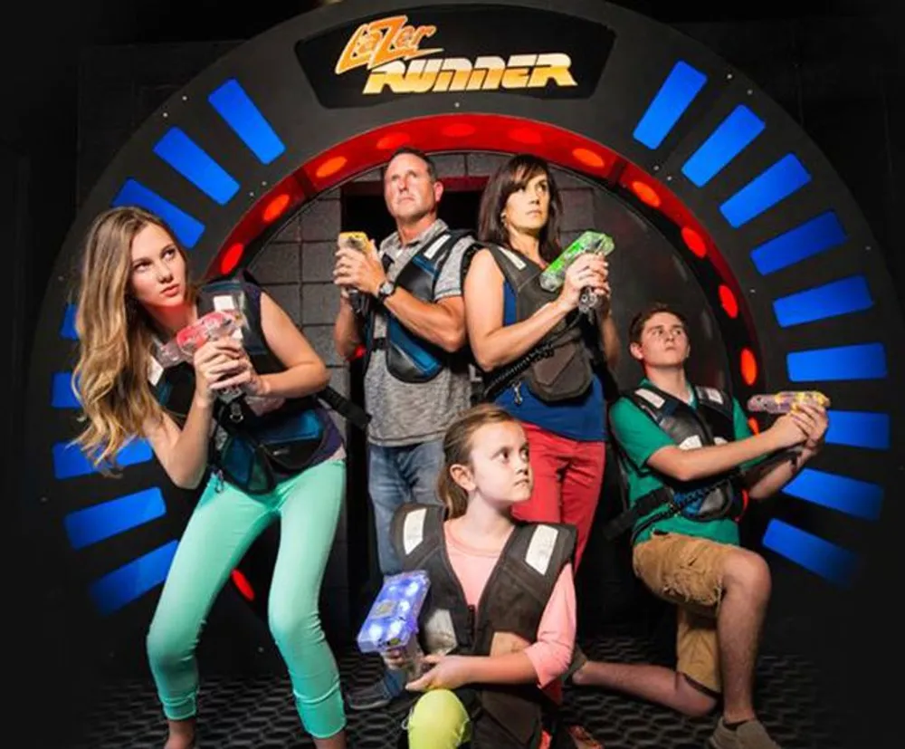 Five people equipped with vests and phasers are posed dramatically in a laser tag arena entrance ready for a game