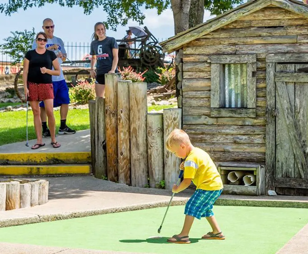 A young boy is playing mini-golf as spectators watch on a sunny day