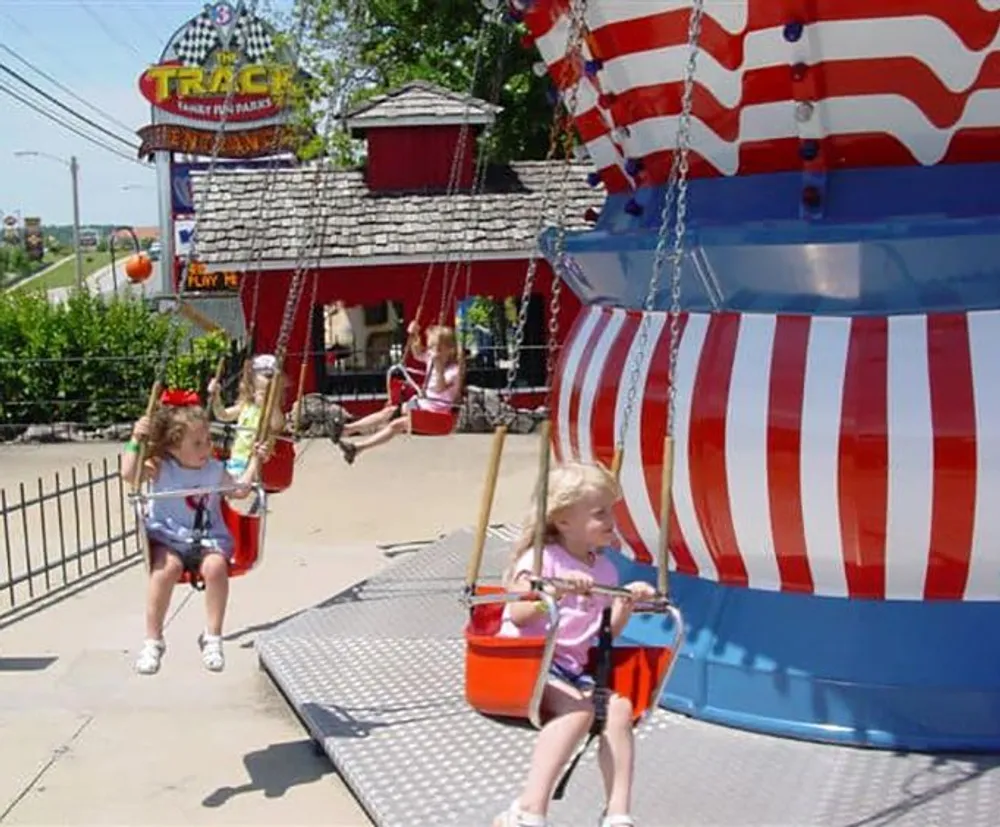 Children are enjoying a swing ride at an amusement park decorated with red and white stripes evoking a festive American theme