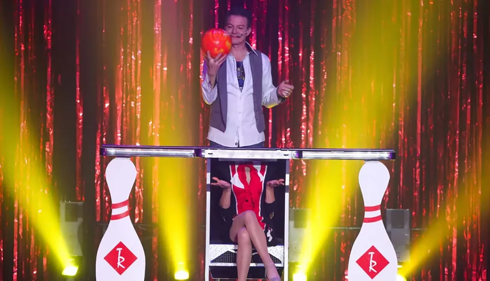 A magician is performing an illusion on stage with a bowling theme splitting themself in half with colorful lighting