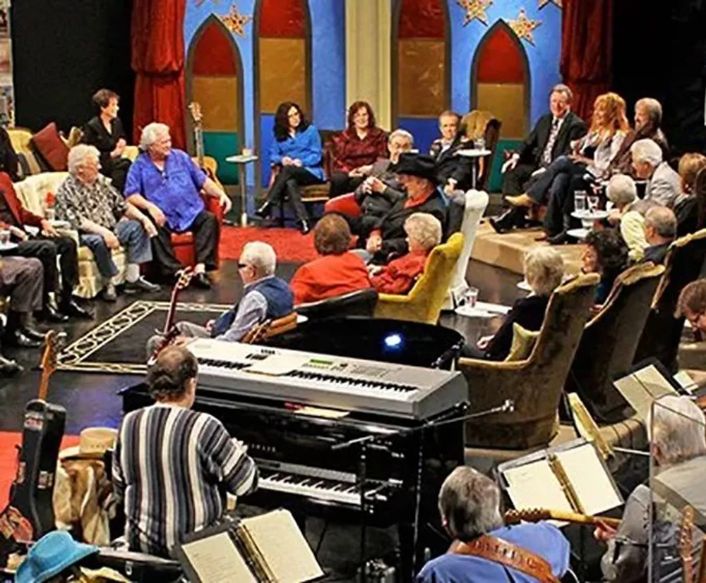 A group of people are gathered in a colorful room many with musical instruments possibly in preparation for a performance or rehearsal